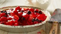 a pie with strawberries and blueberries in it on a table next to a knife