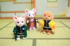 three small toy mice are standing on the floor in front of two other stuffed animals