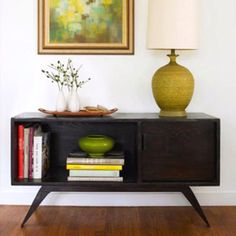 a table with a lamp, vase and books on it in front of a painting