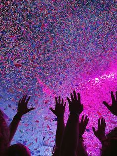 people reaching for confetti in front of a purple and blue wall at a party