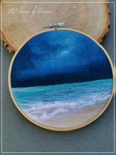 an embroidery project with the ocean and sky painted on it's side, next to a piece of wood