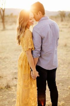 a man and woman standing in the desert holding hands with the sun shining behind them