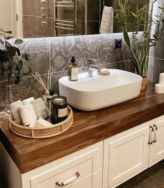 a white sink sitting on top of a wooden counter next to a mirror and potted plant