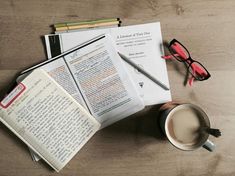 an open book, coffee cup and eyeglasses on top of a wooden table