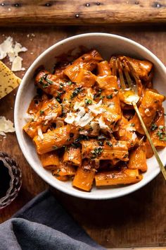 a white bowl filled with pasta and cheese on top of a wooden table next to a fork