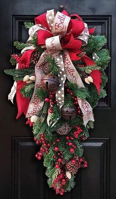 a christmas wreath hanging on the front door with bells and evergreen leaves, red berries and pine cones