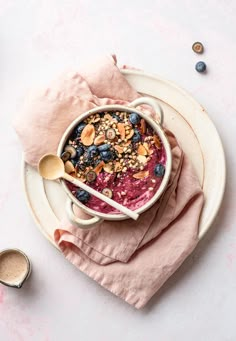 a bowl filled with granola and blueberries on top of a pink napkin next to a spoon