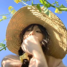 a woman wearing a straw hat and drinking from a yellow flowered bottle in front of a blue sky