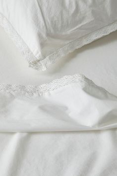 two white sheets with lace on them are laying next to each other in the bed