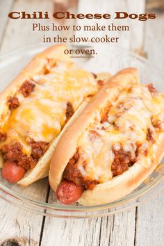 two hot dogs covered in cheese and chili sitting on a glass plate next to each other