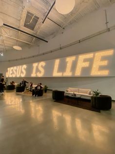 a large sign that says jesus is life in an empty room with people sitting on couches