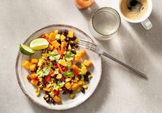 a white plate topped with a salad next to a cup of coffee and an orange slice