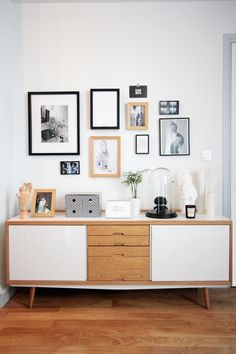 a white and wooden cabinet with pictures on the wall above it, along with other framed objects