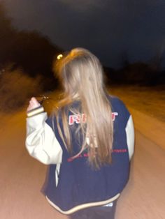 a woman walking down a road at night with her hair blowing in the wind and wearing a blue jacket