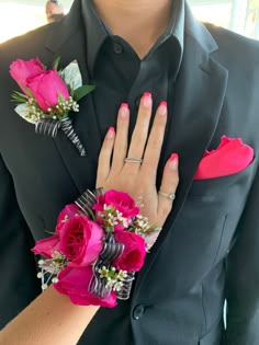 a man in a black suit with pink flowers on his lapel and two silver rings