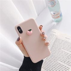 a person holding up a phone case with a cat on it's back and an open book in the background