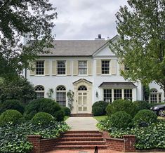 a large white house with steps leading to it's front door and trees in the foreground