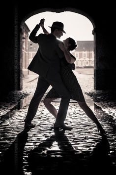 a man and woman dancing in the rain under an arched doorway with their arms around each other