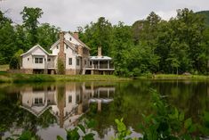 a house sitting on top of a lush green hillside next to a lake in front of a forest