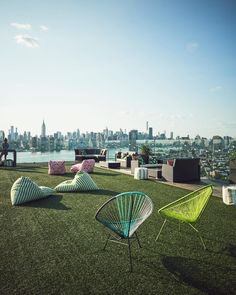 an outdoor lounge area overlooking the city skyline with colorful chairs and pillows on top of it