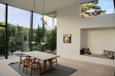 a dining room table and chairs in front of large windows with trees outside the window