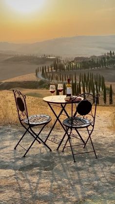 two chairs and a table with wine on it in the middle of an open field