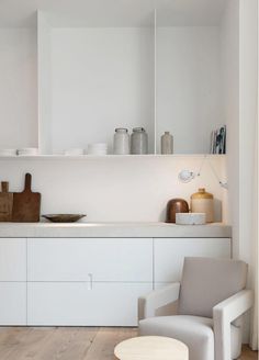 a white kitchen with wooden floors and shelves on the wall, along with a gray chair