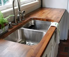 a stainless steel sink in a kitchen with wooden counter tops and wood flooring next to a window