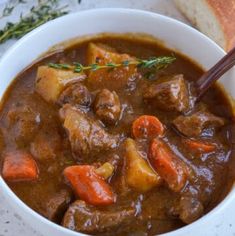 a white bowl filled with meat and carrots next to a piece of bread on top of a table