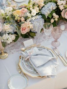 the table is set with plates, silverware and floral centerpieces in pastel colors