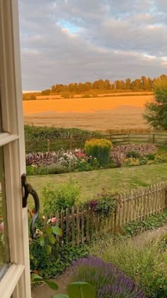 an open window with a view of a field and flowers in the foreground is a wooden fence