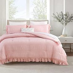 a bed with pink comforter and pillows in front of a window