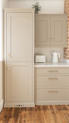 an empty kitchen with white cabinets and wood flooring in front of a brick wall