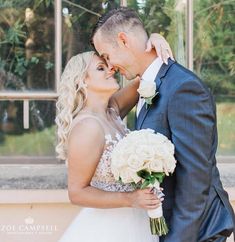 a bride and groom pose for a wedding photo in front of a large glass window