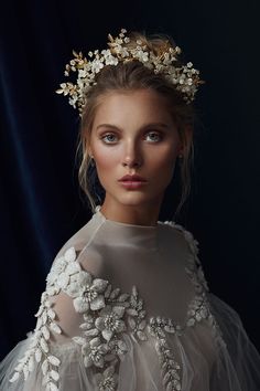 a woman wearing a white dress with flowers on her head and veil over her shoulders