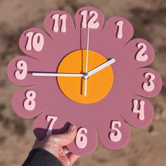 a hand holding a pink clock with numbers on it