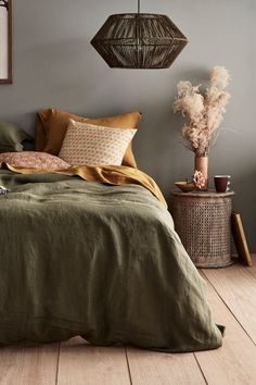 a bed with green linens and pillows in a gray room next to a plant