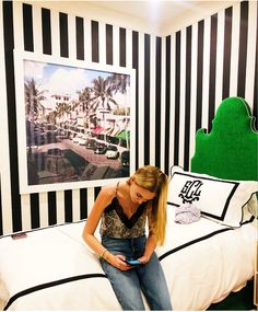 a woman sitting on top of a bed next to a green headboard and black and white striped wall