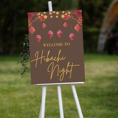 a welcome sign in the middle of a grassy area with flowers and lanterns on it