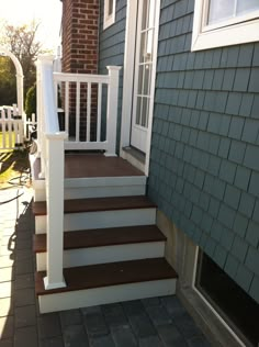 a house with steps leading up to the front door and side porch, next to a brick walkway