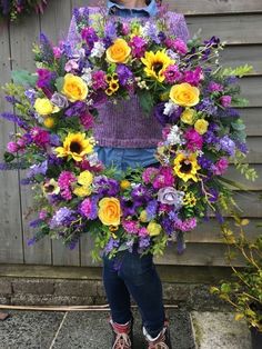 a person holding a wreath with flowers on it in front of a building and fence