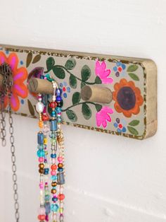 a wall mounted jewelry holder with flowers and chains hanging from it's sides on a white wall