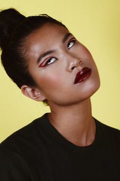 a woman with red lipstick and black shirt looking up at something yellow in the background