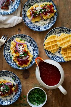 several plates with waffles, sauce and vegetables on them sitting on a wooden table