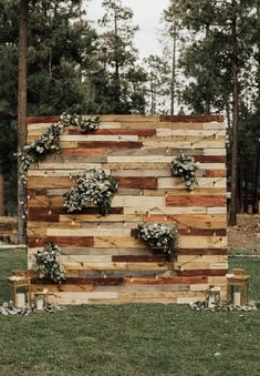 a wooden sign with flowers on it in the middle of a grassy area next to trees