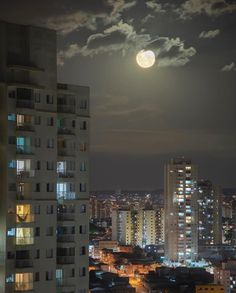 a full moon is seen over the city skyline in this nighttime photo taken from an apartment building