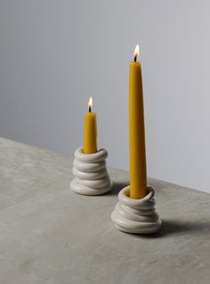 two candles sitting on top of a table next to each other with one candle in the middle