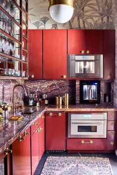 a kitchen with red cabinets and gold trimmings on the counter tops, along with an area rug