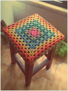 a colorful crocheted stool sits on the floor next to a potted plant