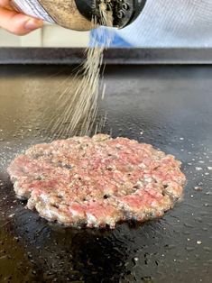 a hamburger being sprinkled with gravy on top of a black counter